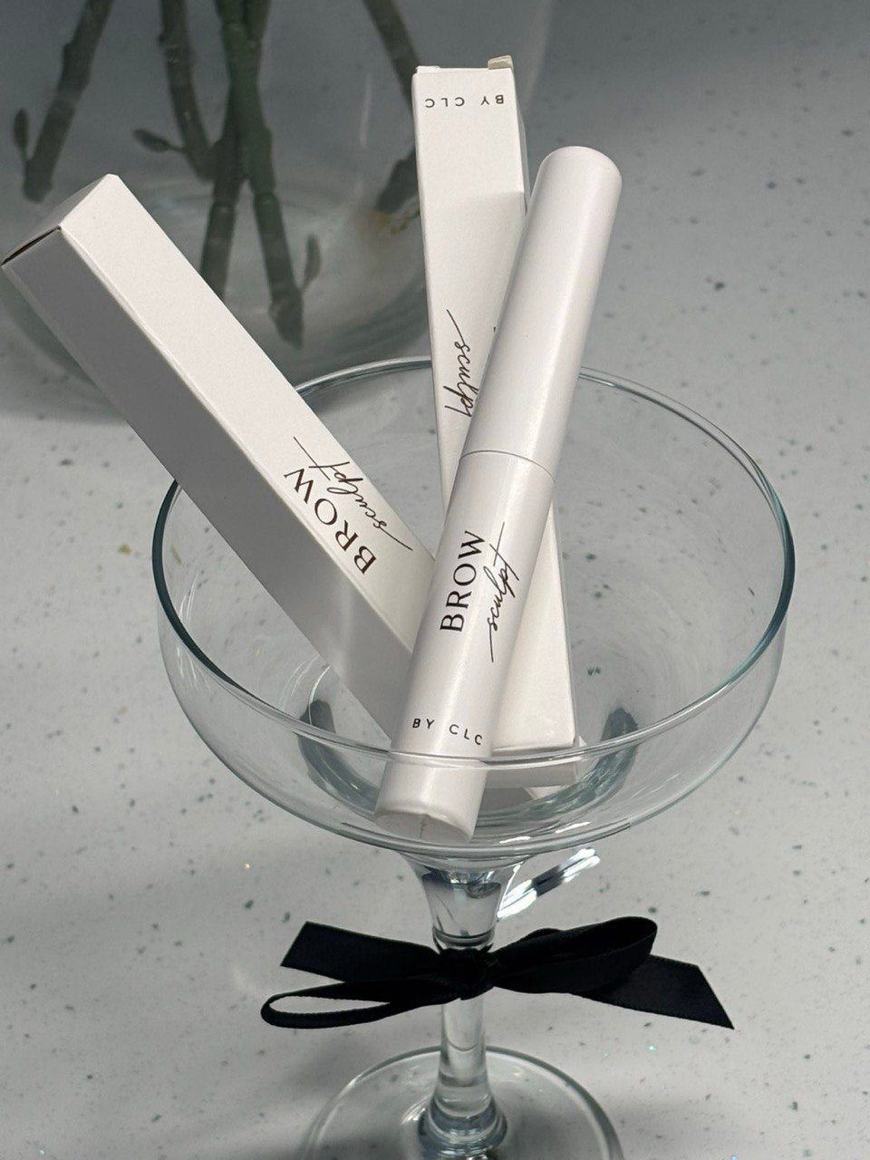 Brow Sculpt tube and boxes in a coupe glass with black bow
